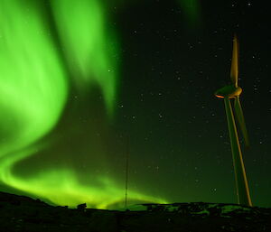 A bright green aurora is visible in the night sky stretching to the horizon. There is a large wind turbine to the right of frame.
