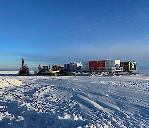 Heavy machinery and shipping containers on an icy plain under a blue sky