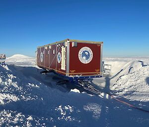 A sled is sitting surrounded by a large building of snow accumulation. This requires clearing the surrounds with a snow groomer before the sled can be moved.