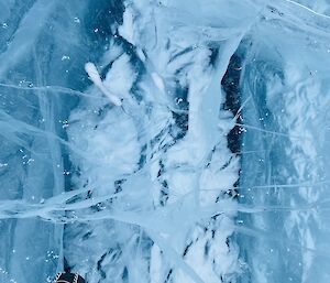 Picture taken looking downwards - two feet in the foreground on frozen lake ice containing white snowy shards of frozen ice.