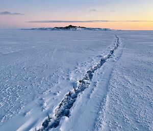 Flat, snow-covered, sea ice with a large extensive crack running through it into the distance.