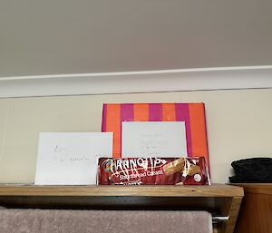 A wrapped present, birthday card, and a packeet of biscuits is sitting on a shelf.