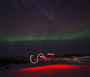 Beneath a night sky lit by a green and purple aurora, a red light has been used to paint the name Cat