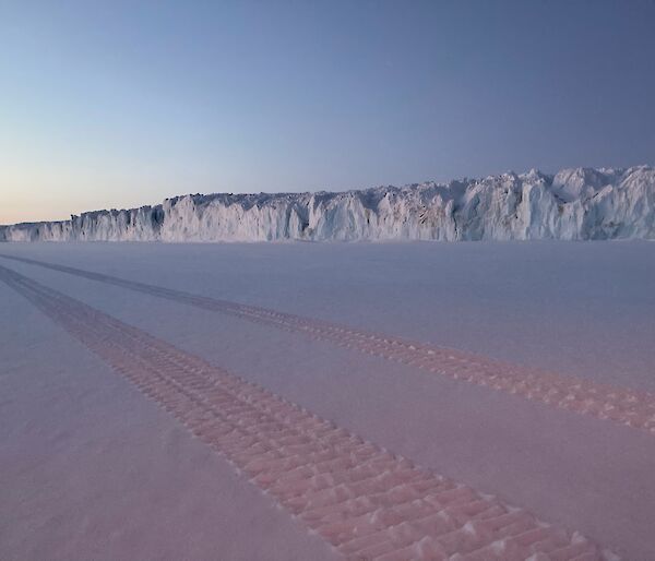 Vehicle tracks in fresh snow with the side wall of a glacier visible in the background.