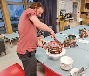 A man is about to cut into a large, multi coloured, birthday cake. The number 40 is on the top of the cake.