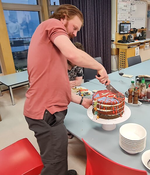 A man is about to cut into a large, multi coloured, birthday cake. The number 40 is on the top of the cake.