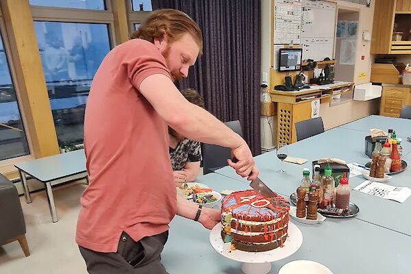 A man is about to cut into a large, multi coloured, birthday cake. The number 40 is on the top of the cake.