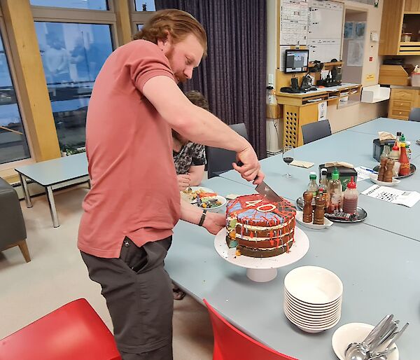 A man is about to cut into a large, multi coloured, birthday cake. The number 40 is on the top of the cake.