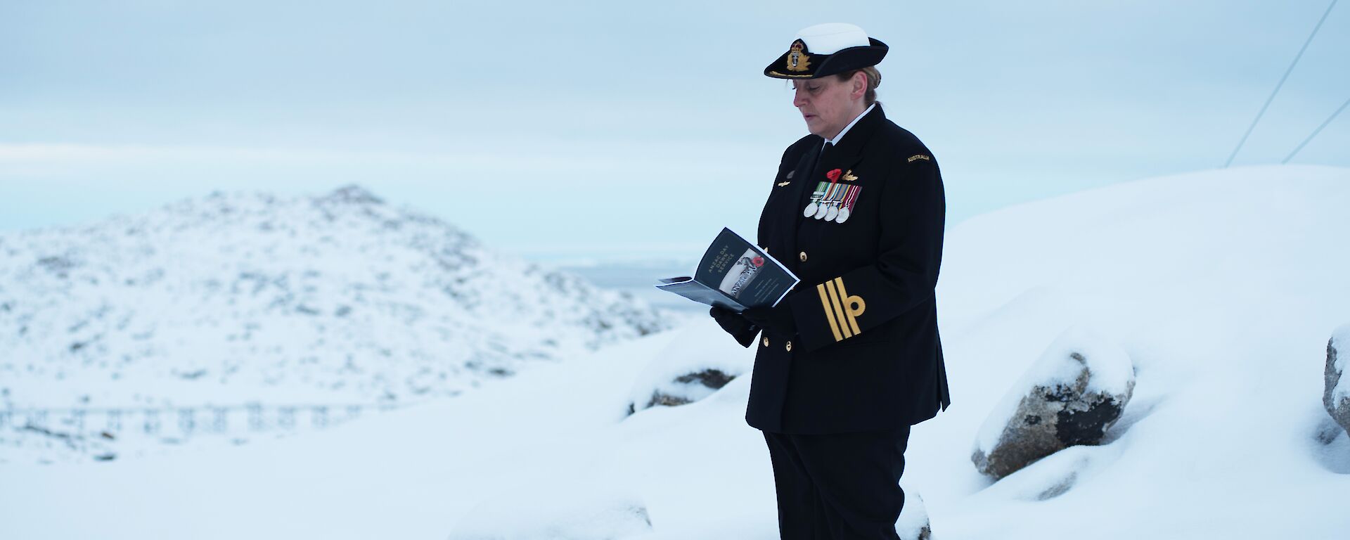 A woman in dark navy dress stands in the snow reading from a program