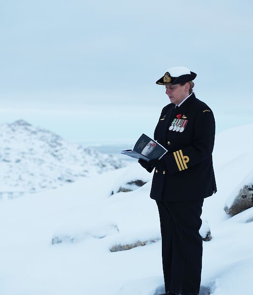 A woman in dark navy dress stands in the snow reading from a program