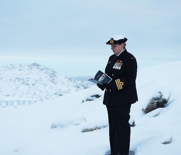 A woman in dark navy dress stands in the snow reading from a program