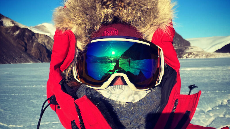 A woman in full snow gear looks at the camera with snow and ice behind her.