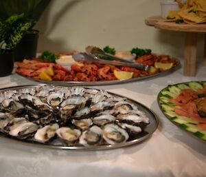 silver trays of oysters, smoked salmon and prawns on a white tablecloth