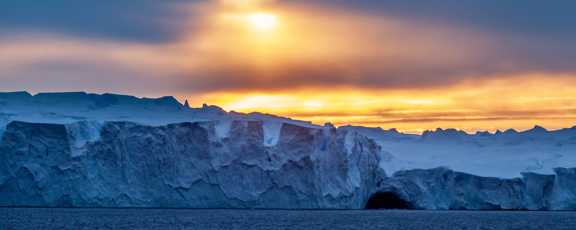 An orange/yellow sunset over a blue ice shelf