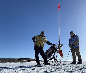 Two men in brightly coloured shirts are standing next to a golf cart on an ice covered harbour