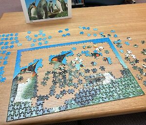 A jigsaw puzzle of penguins is partly complete on a table.
