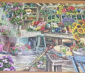 A large jigsaw puzzle of a workshop with many flowers is complete on a table.