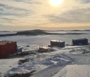 A zoomed out photograph of station buildings and an ice covered harbour. Just visible are a number of people playing golf on the ice.