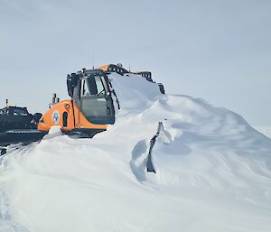 A large yellow snow grooming machine is buried in snow, with just the cabin sticking out.