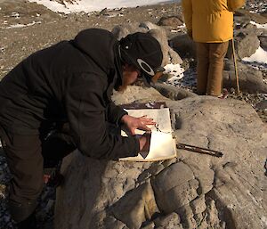 A man is leaning against a rock and signing his name in an old logbook
