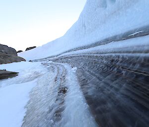 A curved wall of ice rises to the right of frame with a rocky landscape just visible to the left of frame.