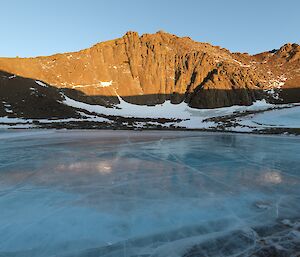 A woman is standing on a large frozen lake. There is a rocky hill rising in the background