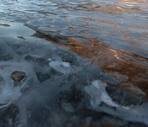 Frozen lake water highlights rocks in a frozen lake. Colours reflect upon the frozen surface.