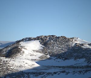 A snow and ice covered rocky island is visible with a large number of emperor penguins gathered in a colony in a hollow formed by the island's hills