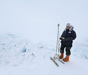 A woman standing on rafted sea ice, beside an instrument to measure snow.