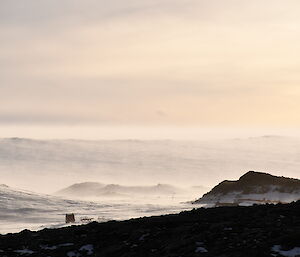 Snow is blowing low over a series of rocky hills, blurring the ground.