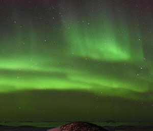 A vivid green band of aurora lights the sky in this panoramic photo. To the left of the photo is a collection of buildings that is Casey Station.