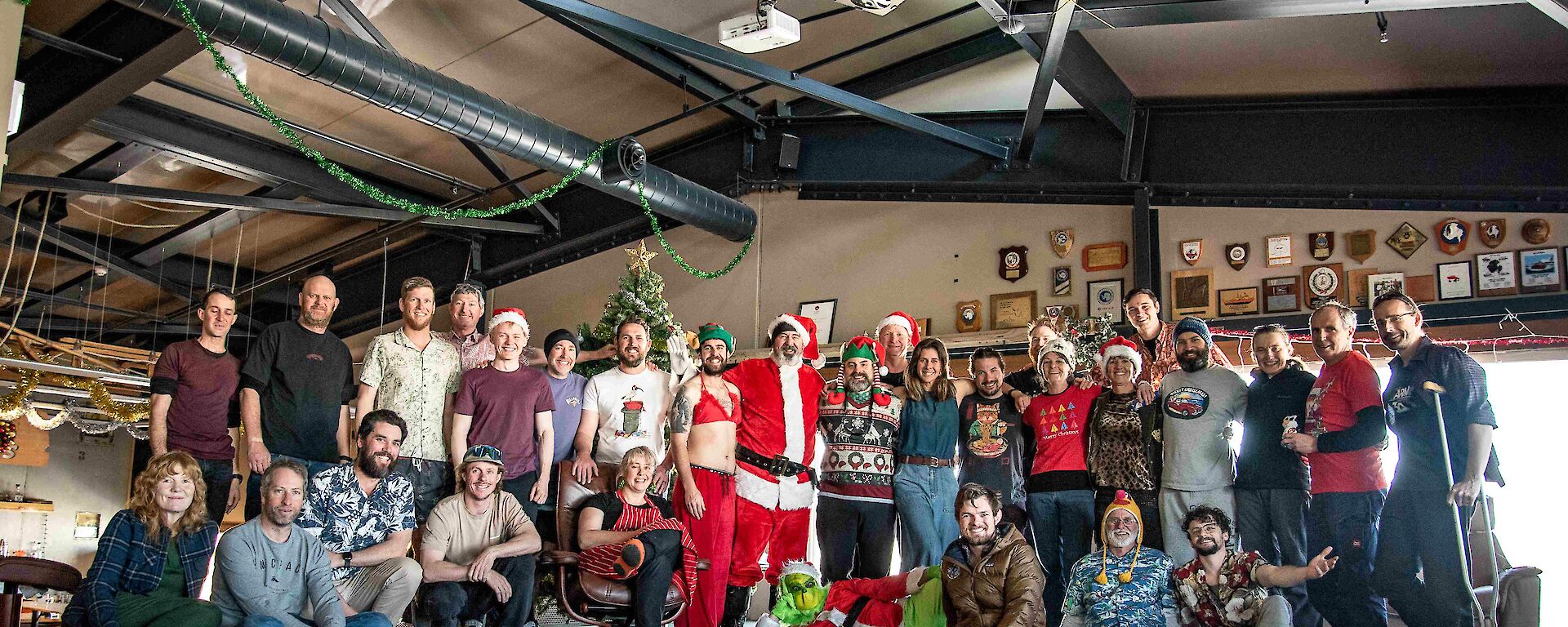 A group of around 30 smiling people in two rows (rear row standing, front row sitting) in front of a Christmas tree