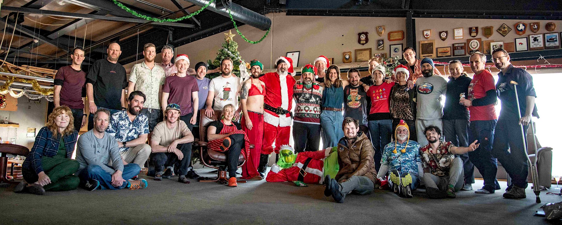 A group of around 30 smiling people in two rows (rear row standing, front row sitting) in front of a Christmas tree