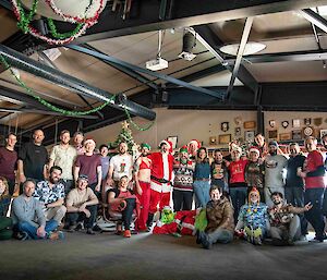 A group of around 30 smiling people in two rows (rear row standing, front row sitting) in front of a Christmas tree