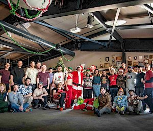 A group of around 30 smiling people in two rows (rear row standing, front row sitting) in front of a Christmas tree