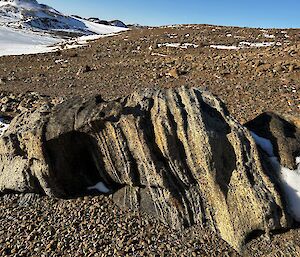 A rocky, ice covered, landscape with a large rock in the centre of frame which has been worn by millenia of wind