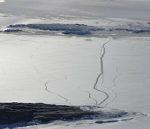 A large crack can be seen in the sea ice running between two rocky islands. There are smaller cracks extending each side of the main crack.