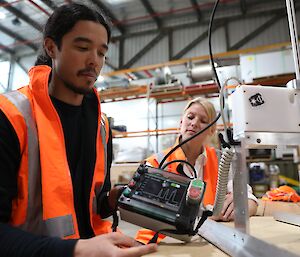 A man and woman in high visibility vests with a snow measuring instrument.