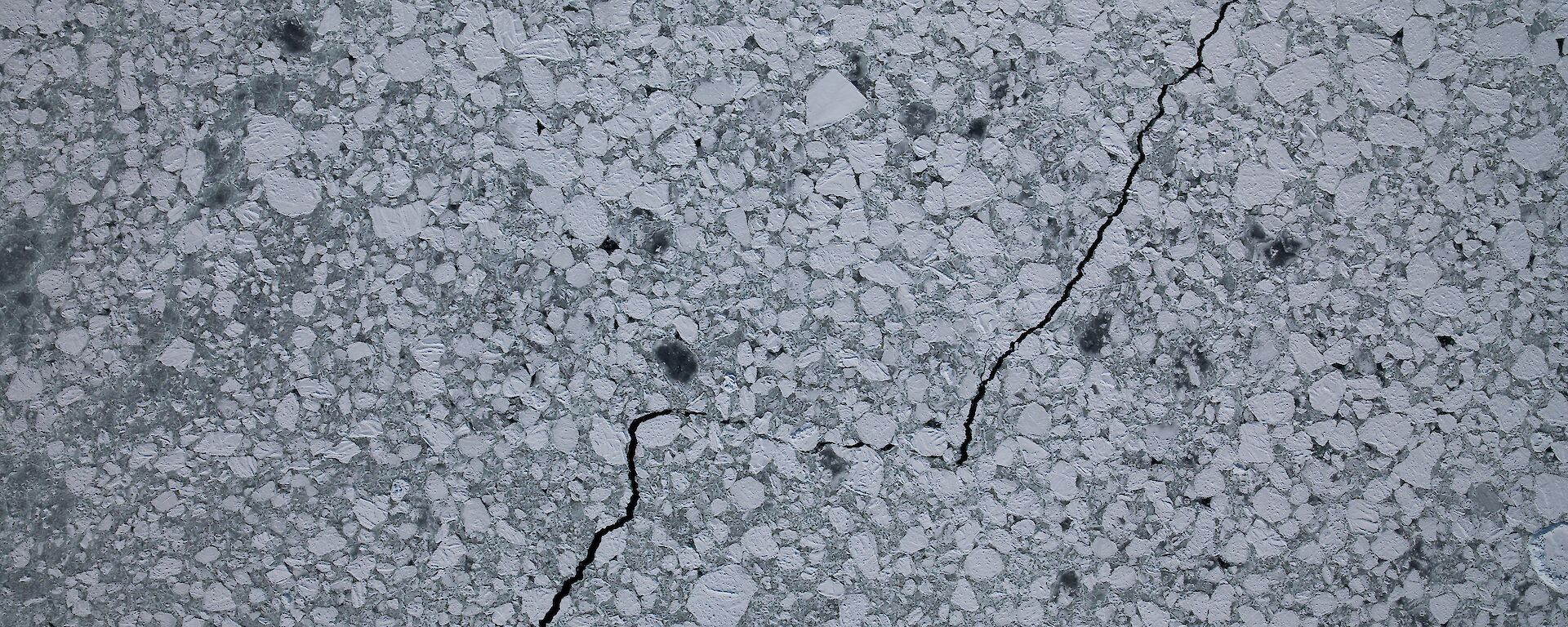 Aerial view of white pancakes of sea ice on a grey ocean.