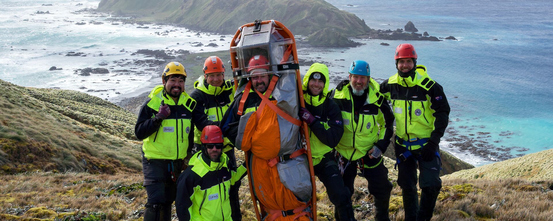 A group stand on a hill in bright yellow high vis, with one person tied in to a stretcher