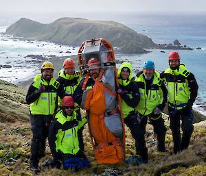 A group stand on a hill in bright yellow high vis, with one person tied in to a stretcher