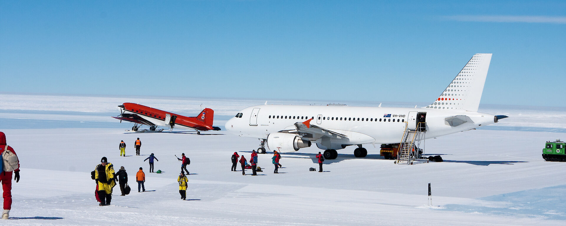 A white airplane on the ice runway with a red small plane in the distance and passengers walking off