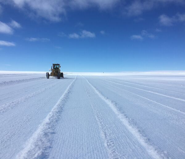 A tractor works on ice under a deep blue sky.