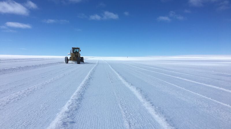 A tractor works on ice under a deep blue sky.