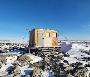 A rustic hut standing on a rocky snow covered ground.