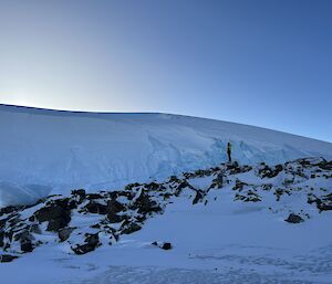 A snow-covered rocky outcrop with a snow-covered icy plateau towering behind it.