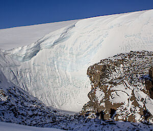 An ice cliff about 50 metres high towers over a snow covered rocky outcrop.