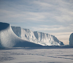 Sea-ice in the foreground, sculpted and wind scoured icy ridge in the midground and a large tabular iceberg with the sun glistening of its cliff-like face in the background.