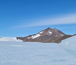 A wave of ice is on the right of frame on an ice plateau. In the distance is a rocky mountain rising from the ice.