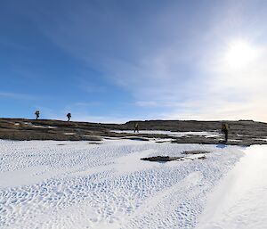 Four men are walking across a rocky, ice and snow covered, hillside.